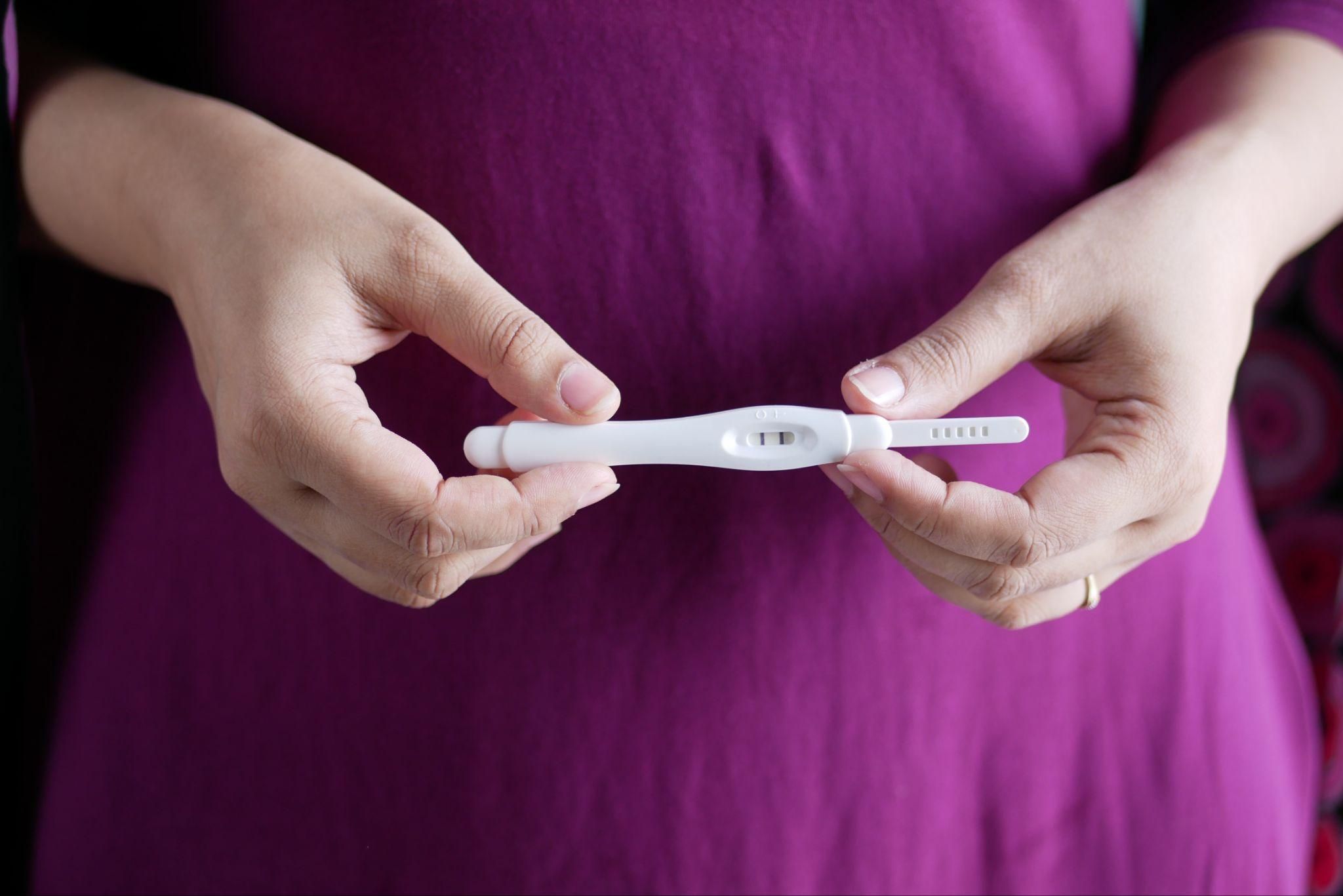 A pregnancy test displaying positive results beside a bottle of antenatal vitamins.