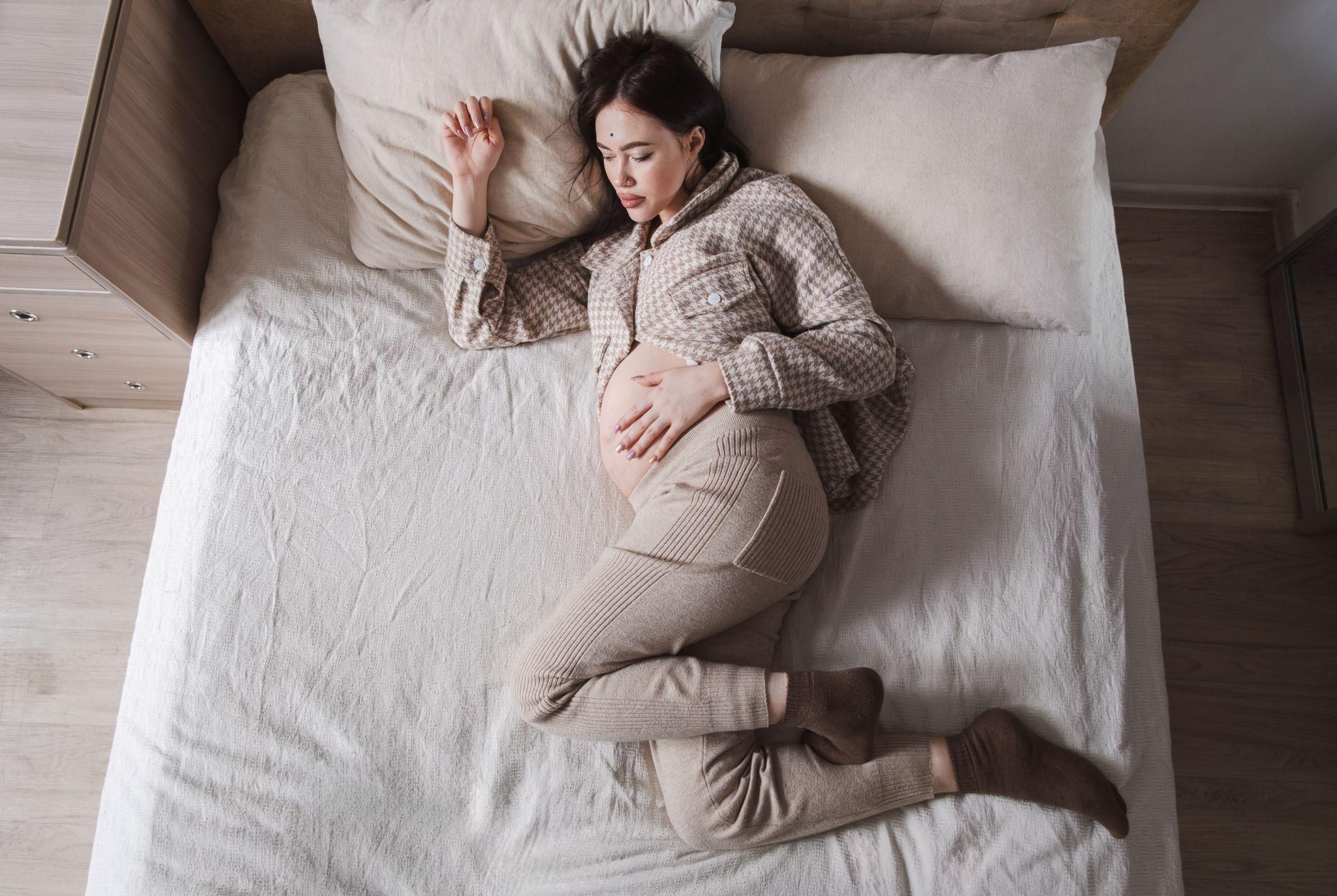 A pregnant woman in bed, holding her stomach, dealing with heartburn.