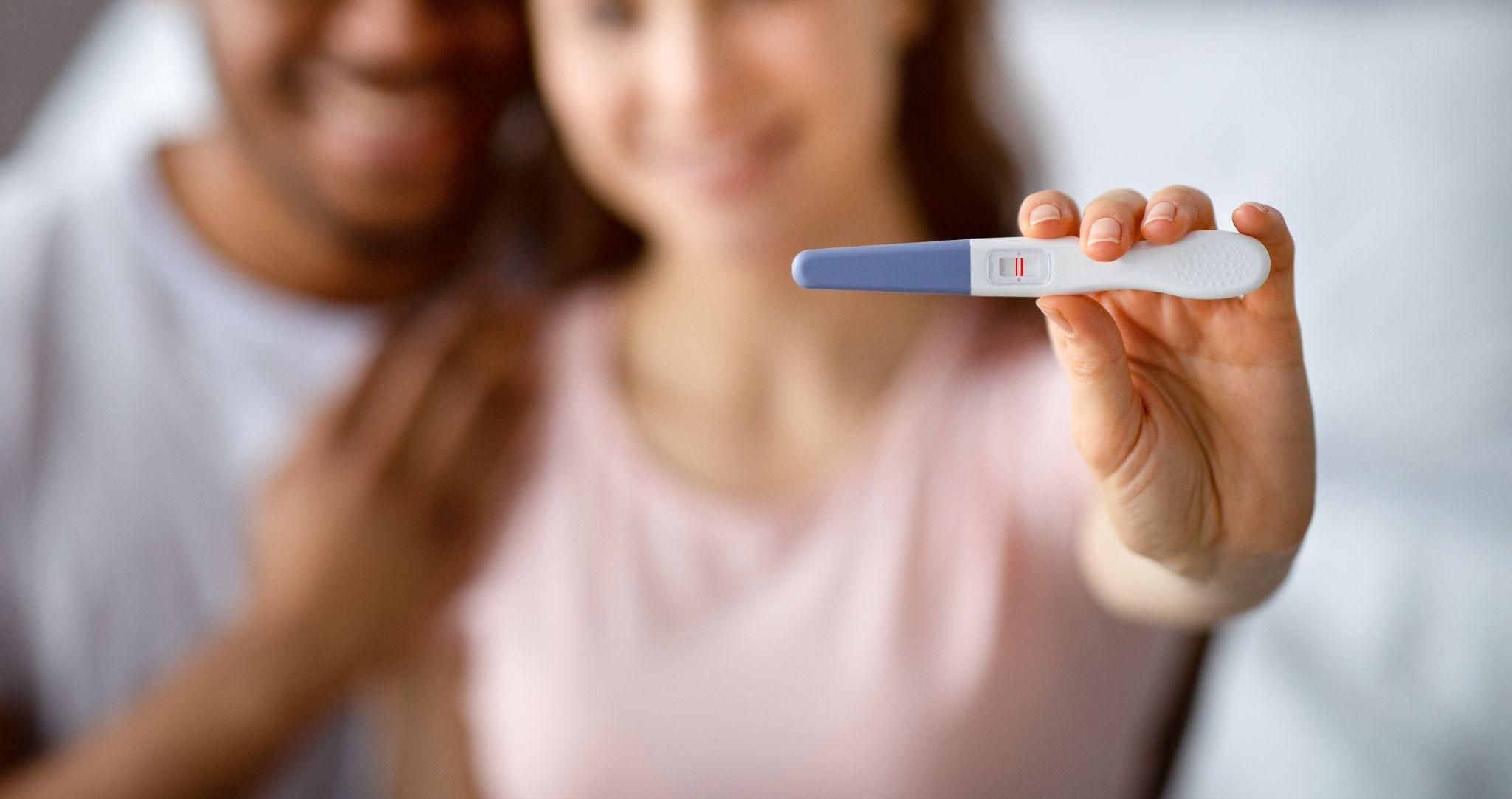 A pregnancy test showing positive results next to antenatal vitamins and a small flower.