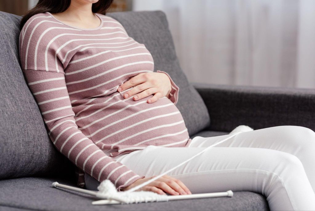 Pregnant woman manages stress and anxiety by knitting on the couch.