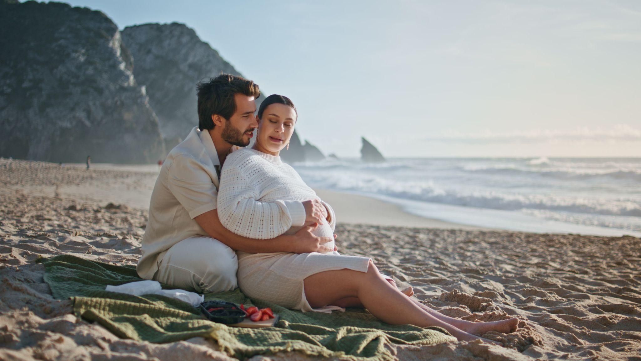 Pregnant woman and her partner enjoying a beach holiday for their babymoon.