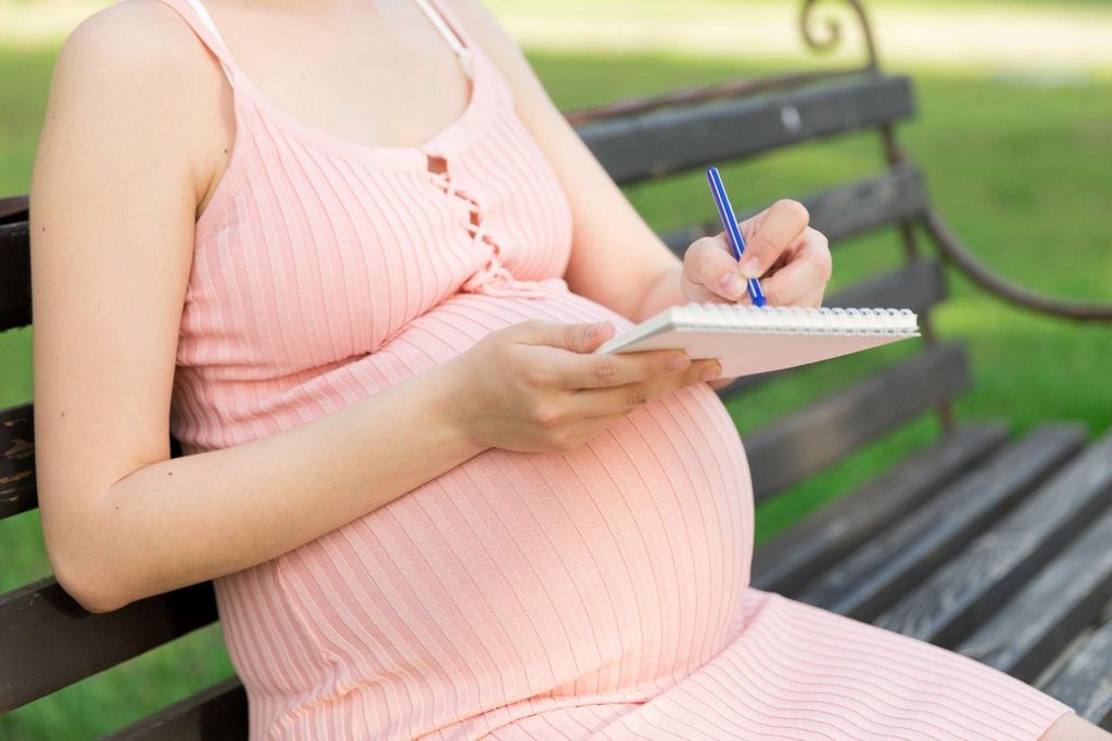 A pregnant woman writing her antenatal birth plan while sitting on a comfy bench.