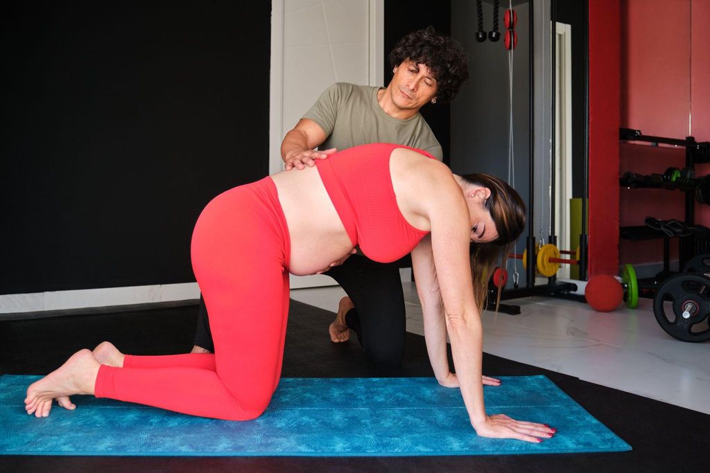 A smiling pregnant woman performing a Cat-Cow stretch to improve antenatal posture.