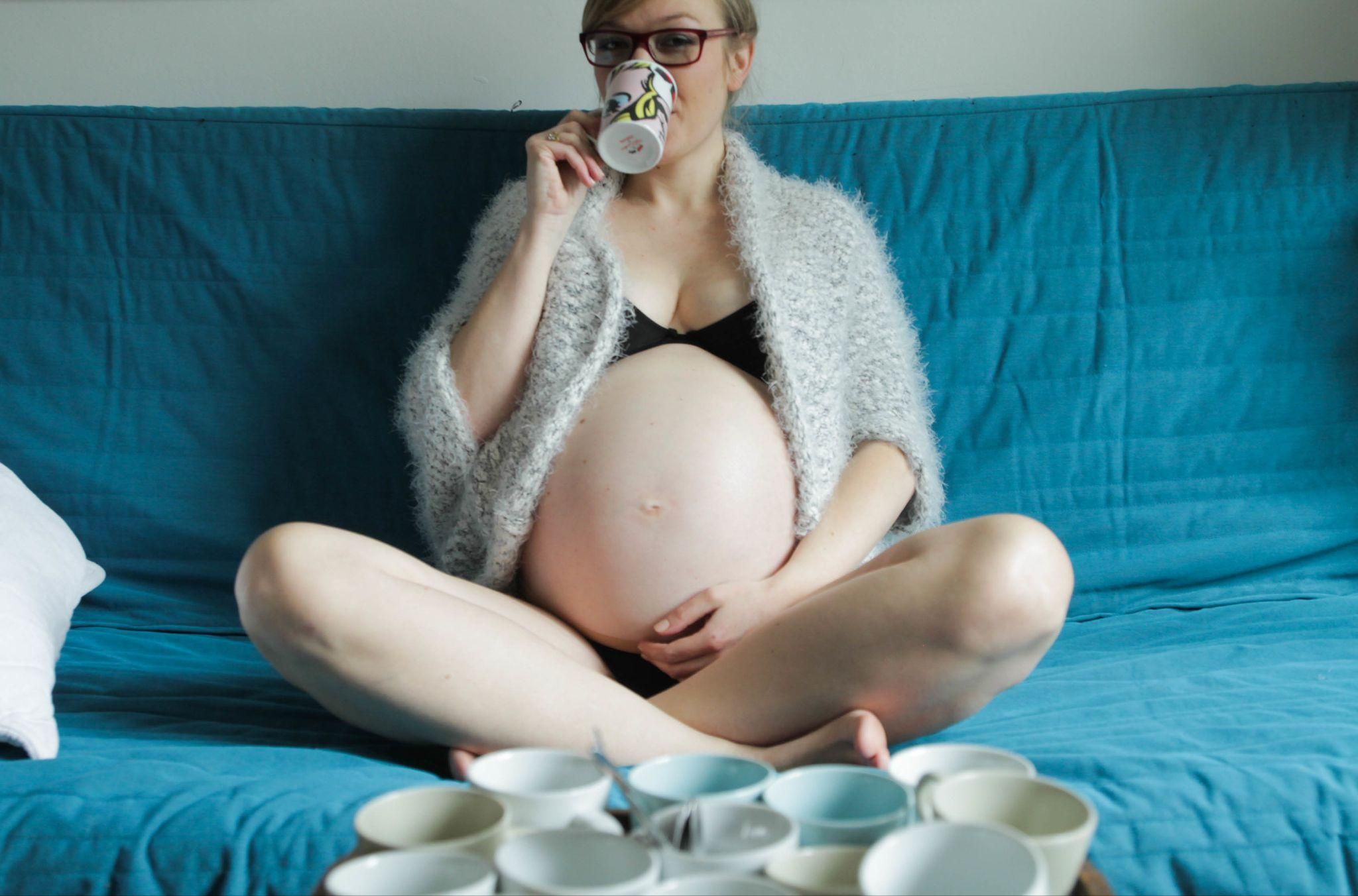 Heavily pregnant woman sits and drinks tea at home.