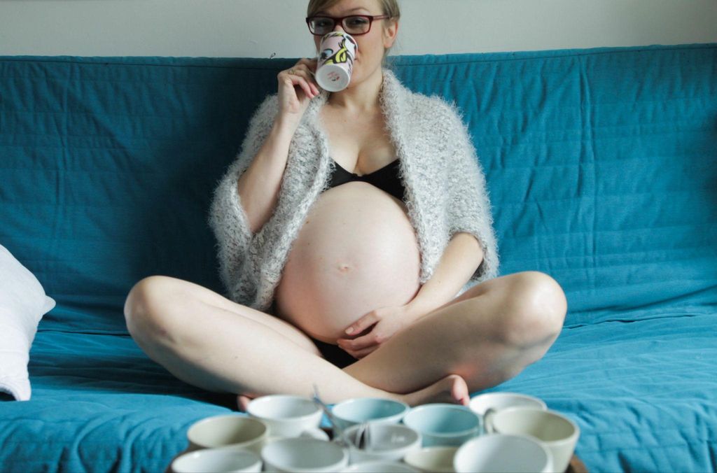 Heavily pregnant woman sits and drinks tea at home.