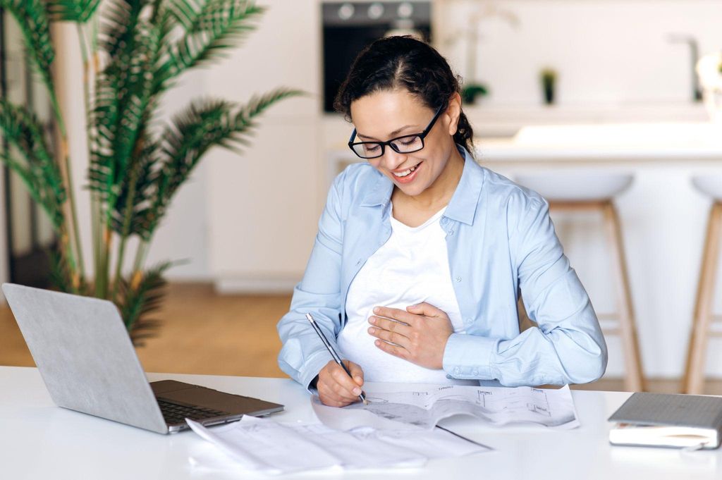 Expecting parent budgeting for baby essentials using a laptop and notepad.