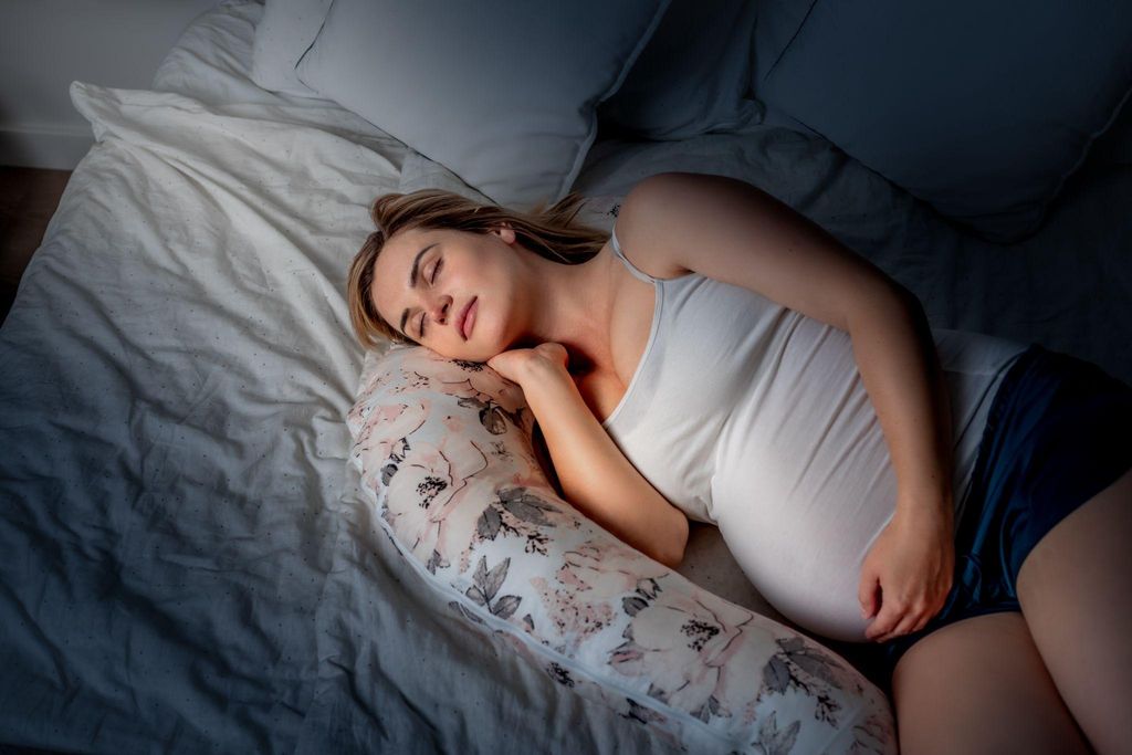 A pregnant woman sleeping on her side using a U-shaped pregnancy pillow.