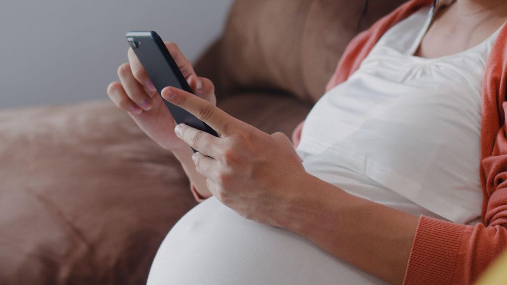 Pregnant woman researching antenatal symptoms on her phone.