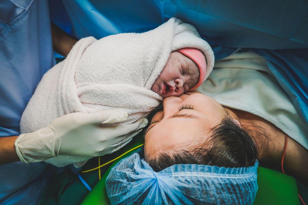 A smiling mother recovering from a C-section, cradling her newborn baby in her arms.