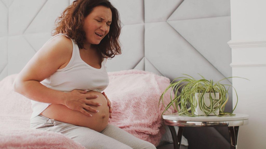 A pregnant woman suffering from abdominal pain sits on her bed.