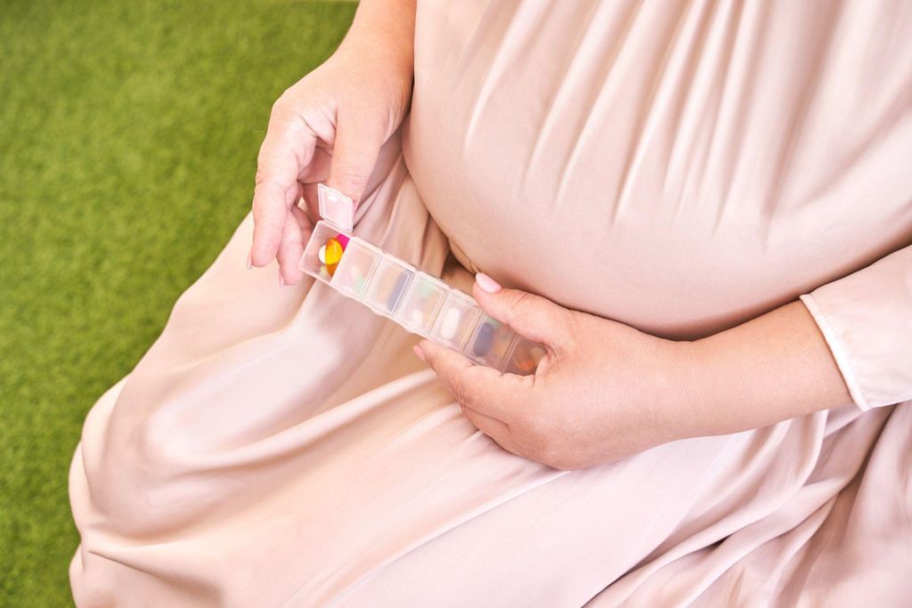 Pregnant woman with pink dress puts antenatal vitamins in pill organiser.