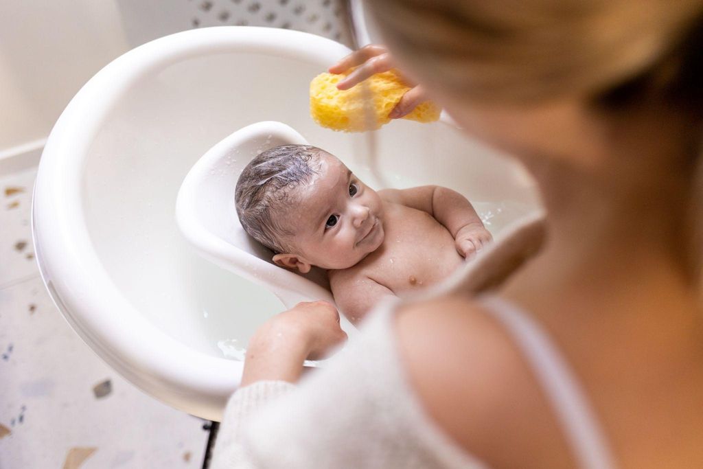 A baby being bathed in a kitchen sink with gentle, warm water.