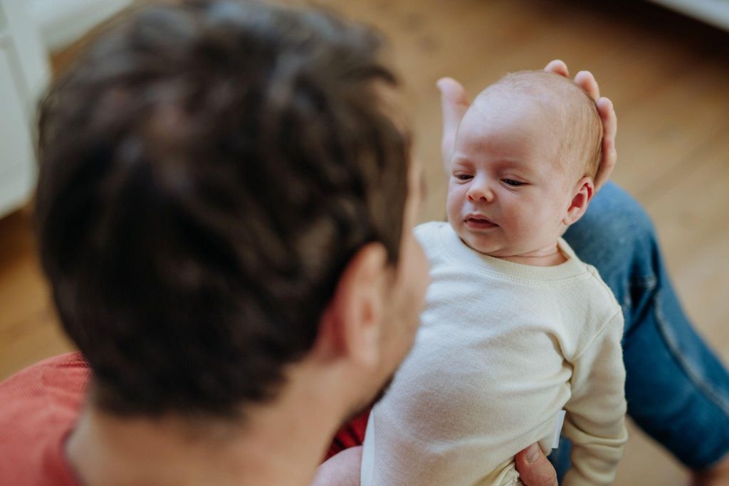 A father bonding with his newborn during the fourth trimester, with his partner resting nearby.