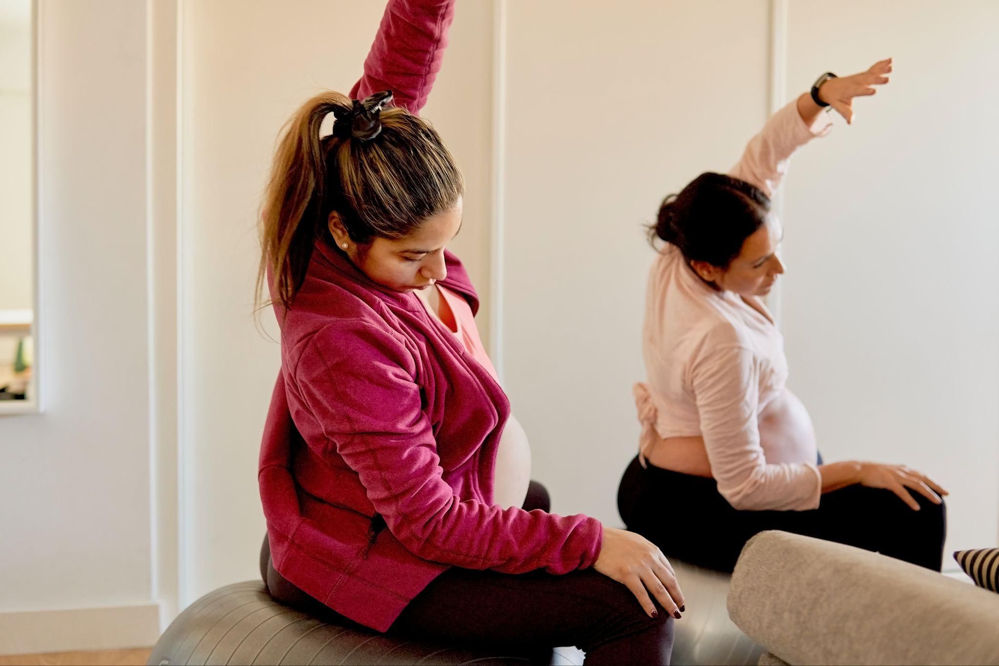 A pregnant woman on a birthing ball performing a yoga stretch to support proper antenatal posture.