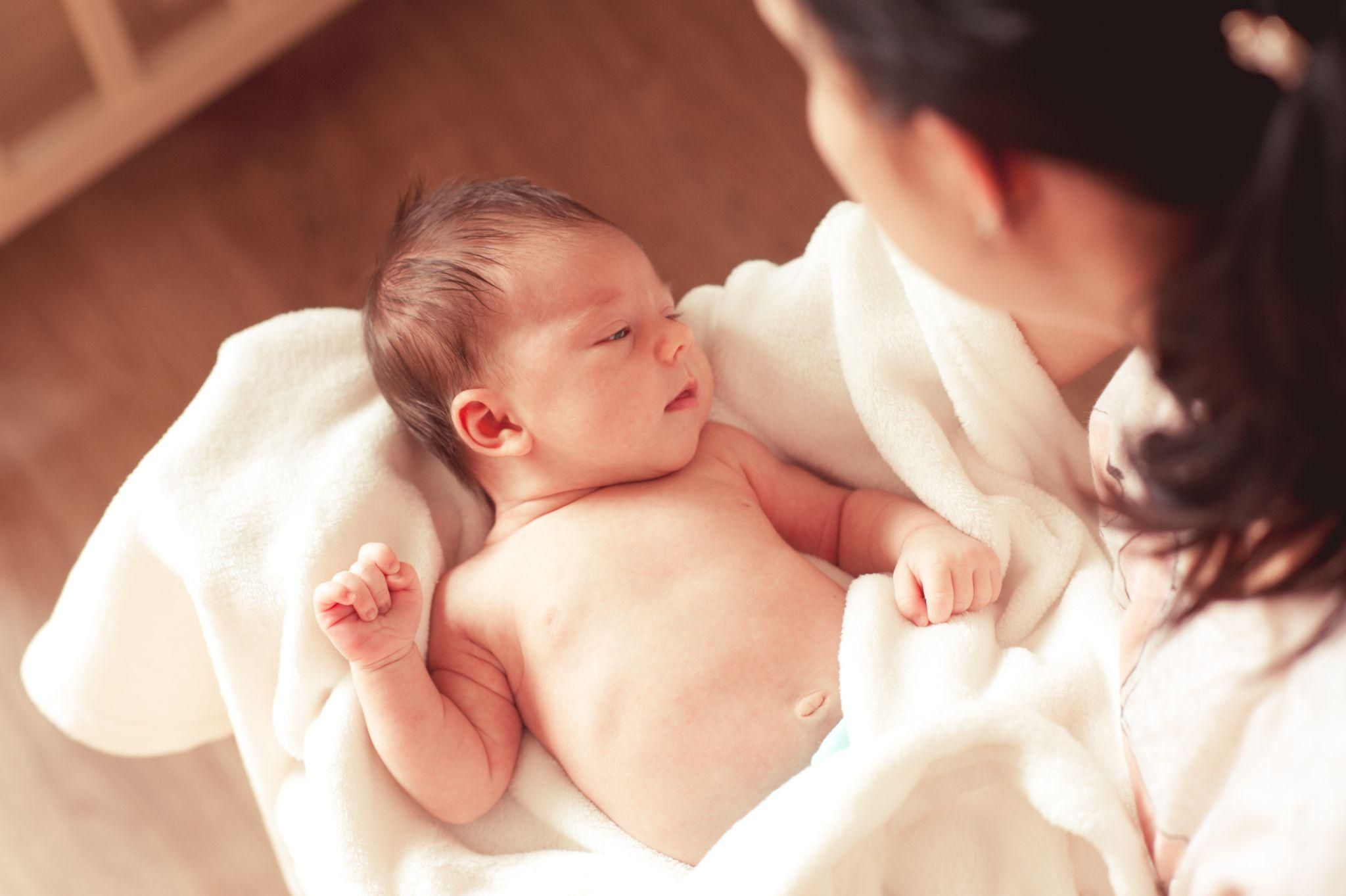 A mother breastfeeding her newborn baby while looking tired and overwhelmed.