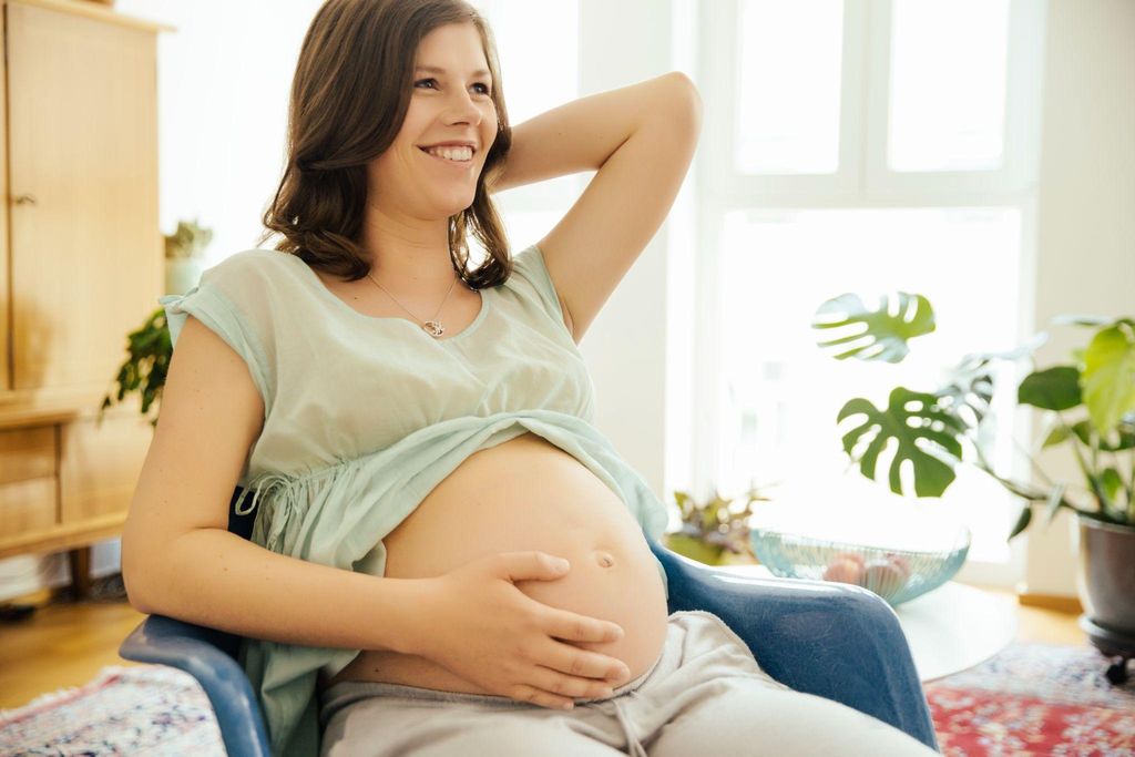 Pregnant woman in conversation with partner or family member. Smiling and happy.