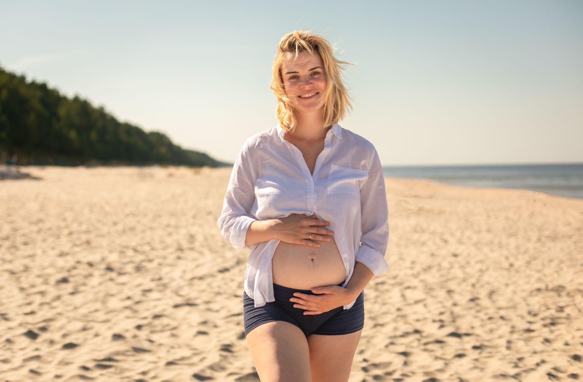 Pregnant woman walking on beach.