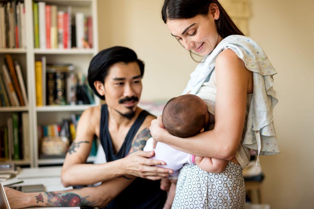 A supportive father helping his wife by caring for their baby while she relaxes.