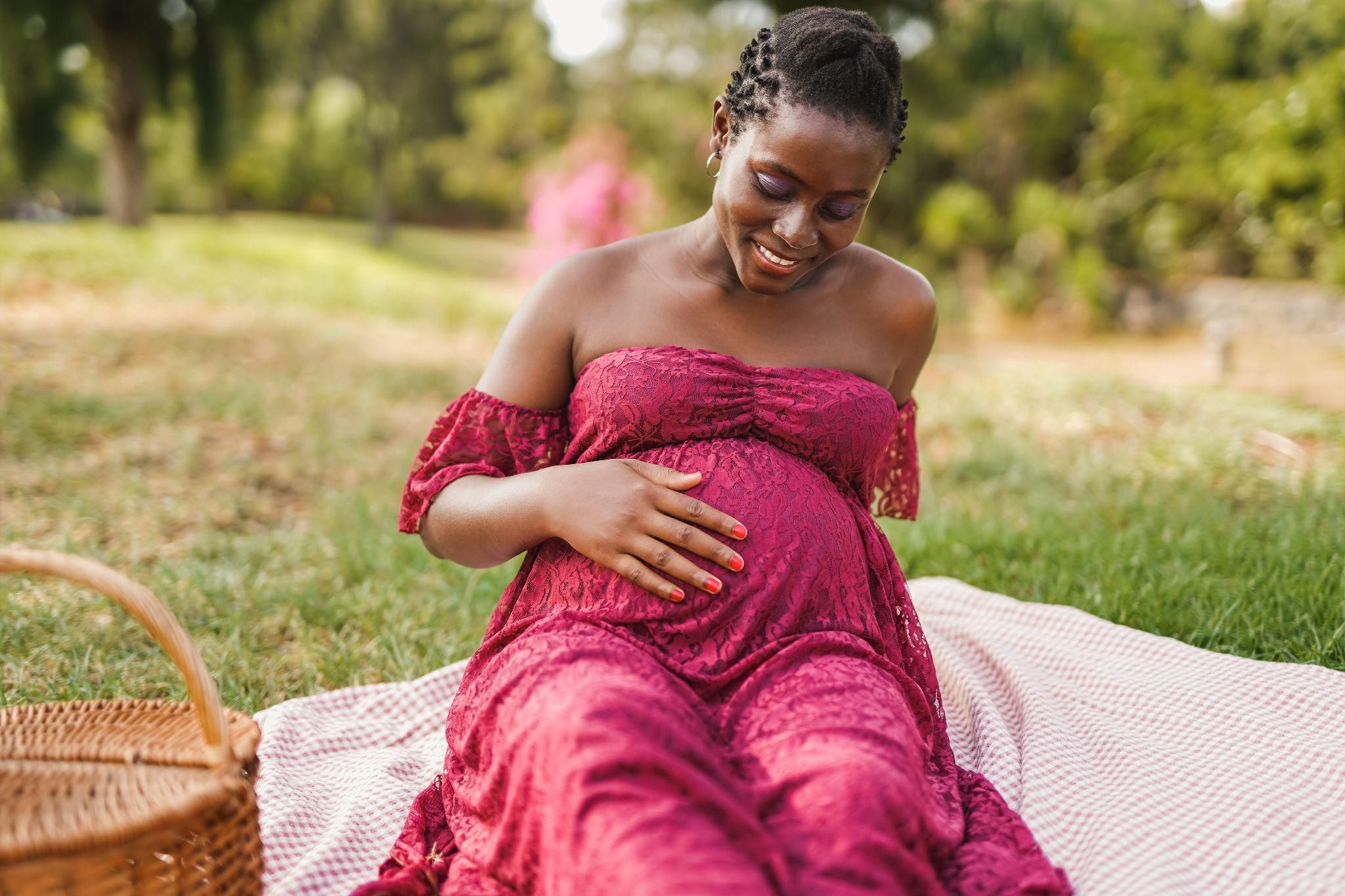 Pregnant lady sits in park with hand over belly.