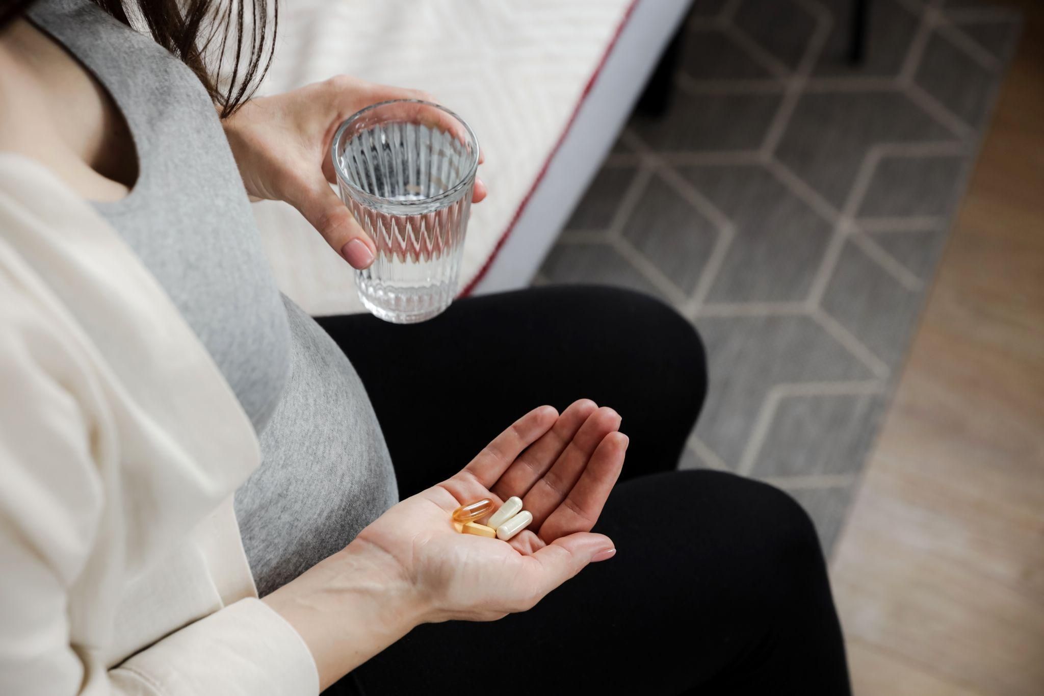 Vitamins with a smiling pregnant woman holding her belly in the background.