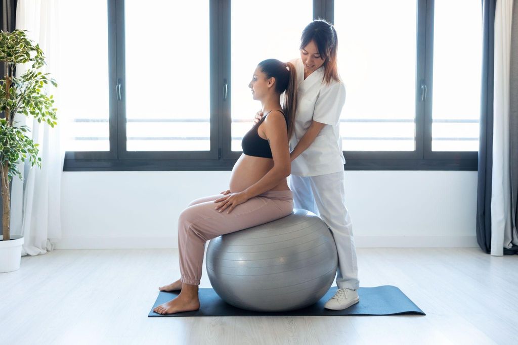 A smiling pregnant woman sitting upright with proper antenatal posture on a yoga ball.