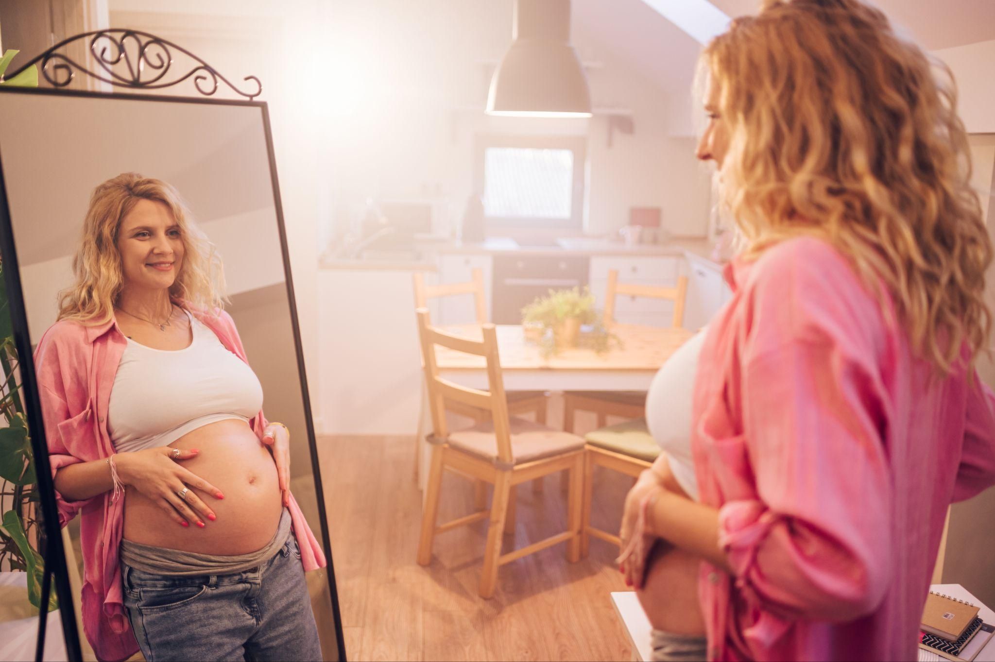 Pregnant woman examines bump in mirror at 28 weeks pregnant.