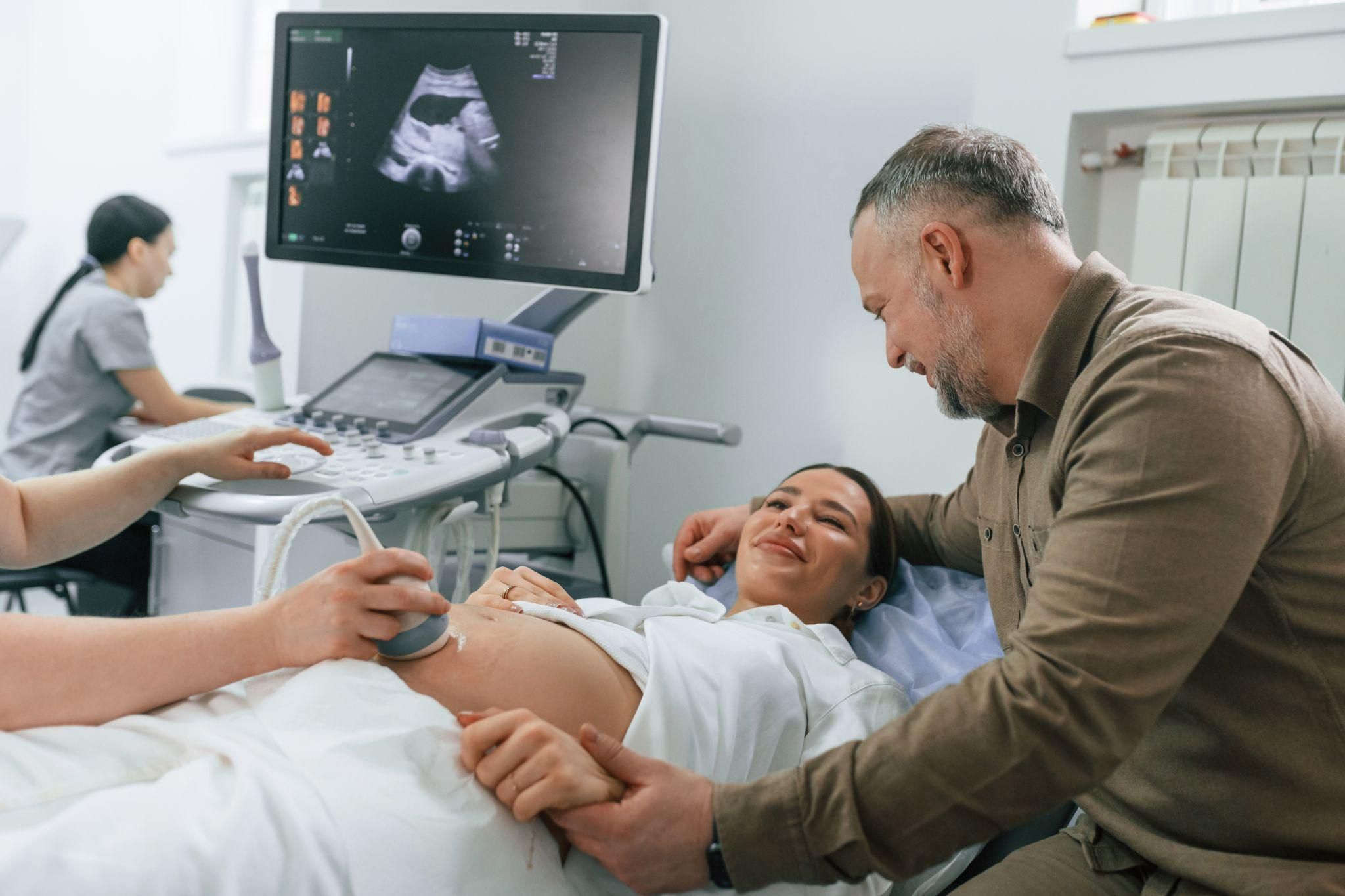 Pregnant woman smiling as a midwife checks her baby’s heartbeat during an antenatal visit.