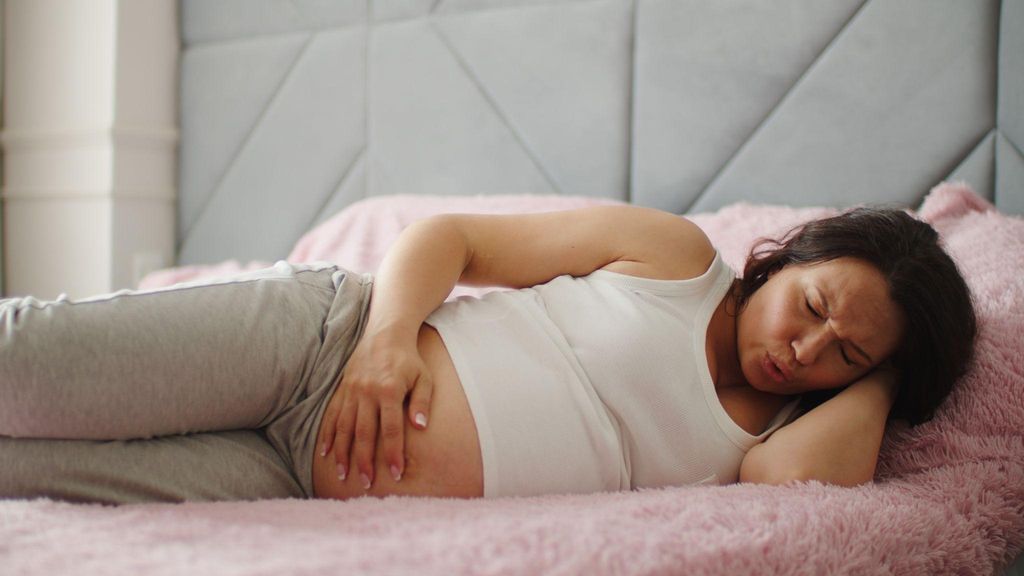 A pregnant woman with a large bump is suffering from abdominal pain and lying on her side.