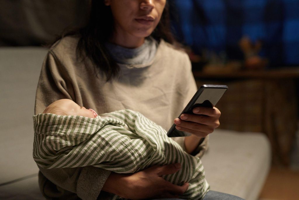 A mother cradling her baby while browsing her smartphone.