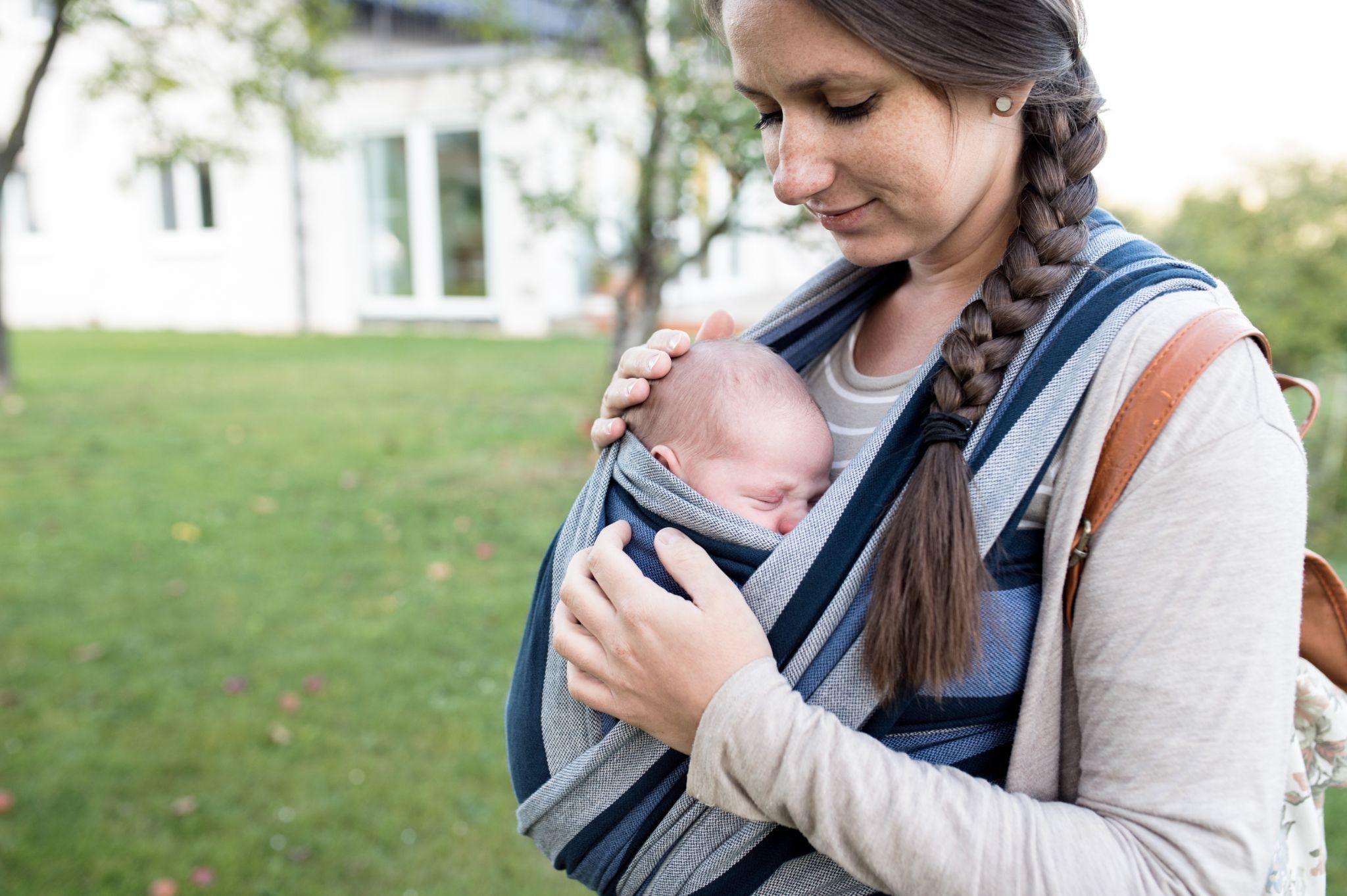 A mother wearing a baby sling during an outdoor walk.