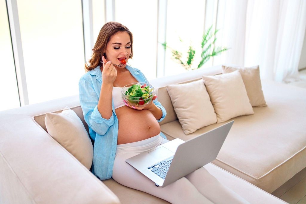 A smiling pregnant woman eating a healthy salad and drinking water.