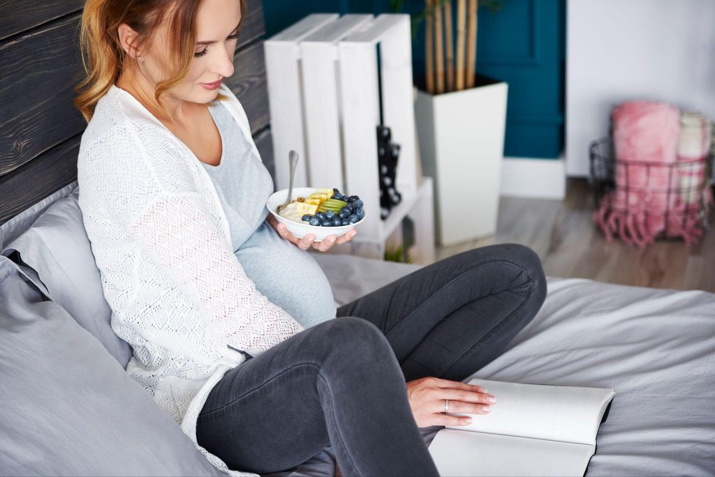 "Pregnant woman reading a novel in a relaxing environment with a warm drink."