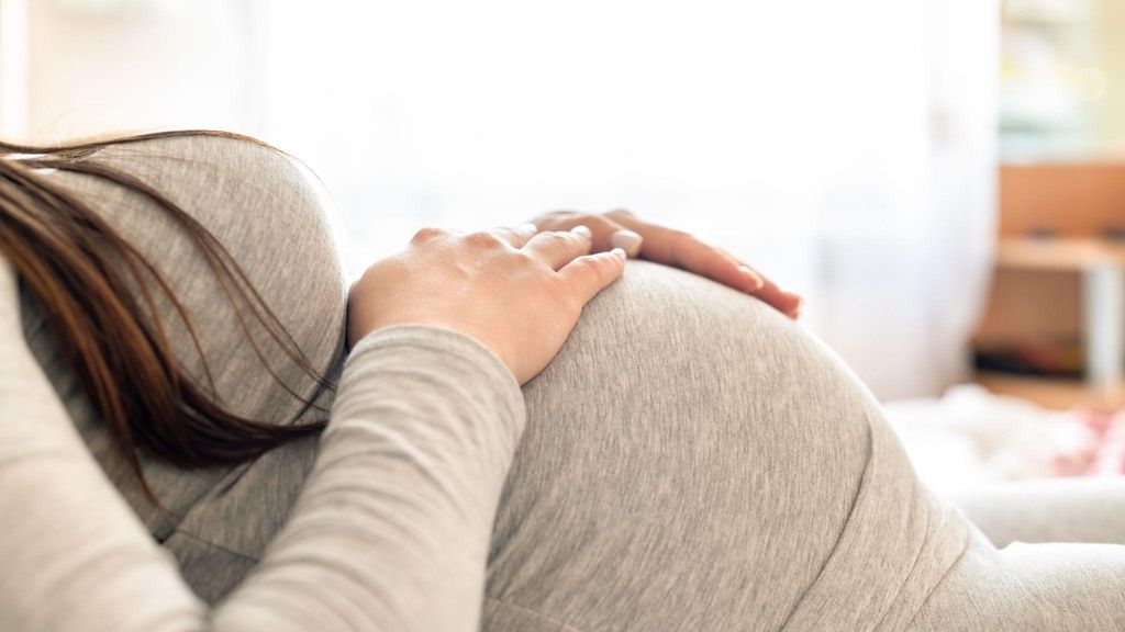 Pregnant woman sitting on a yoga mat, touching her belly, looking thoughtful and serene.