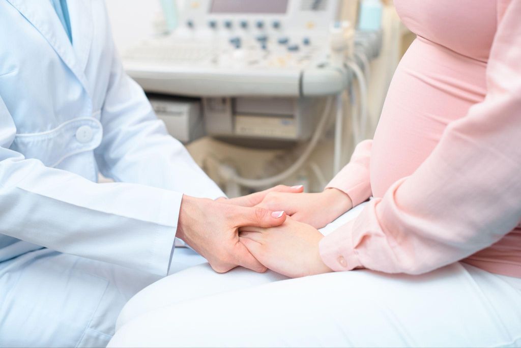 Obstetrician and gynaecologist holds pregnant woman’s hands during antenatal clinic appointment.