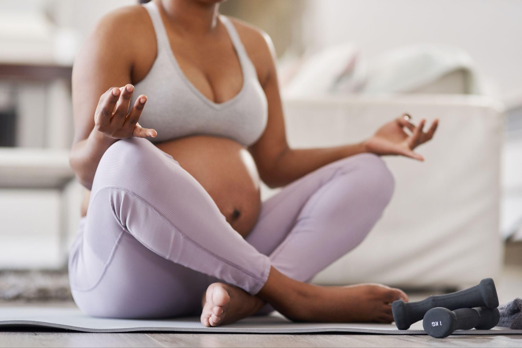 A pregnant woman smiling while practising yoga at home.