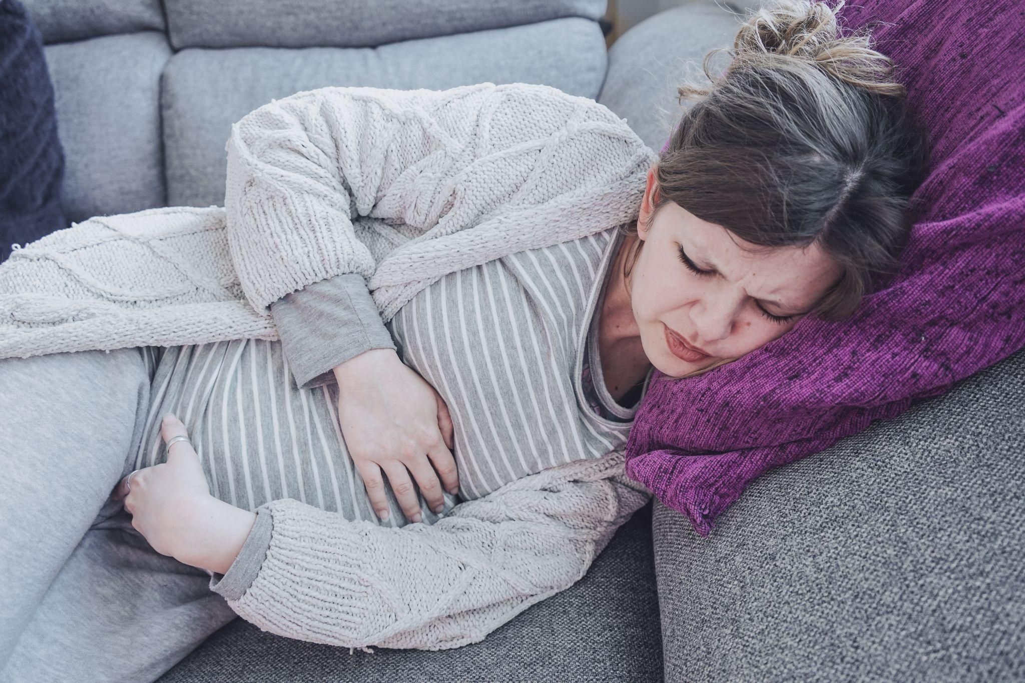 Pregnant woman suffering from abdominal pain lies on her side on the sofa.