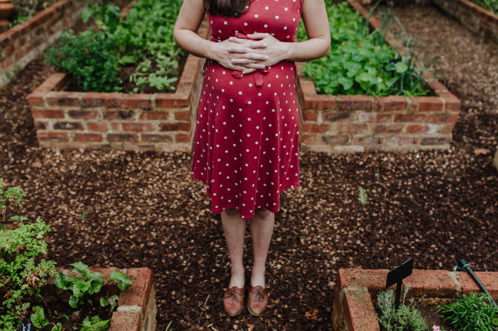 Pregnant woman in spotted red dress enjoys garden.