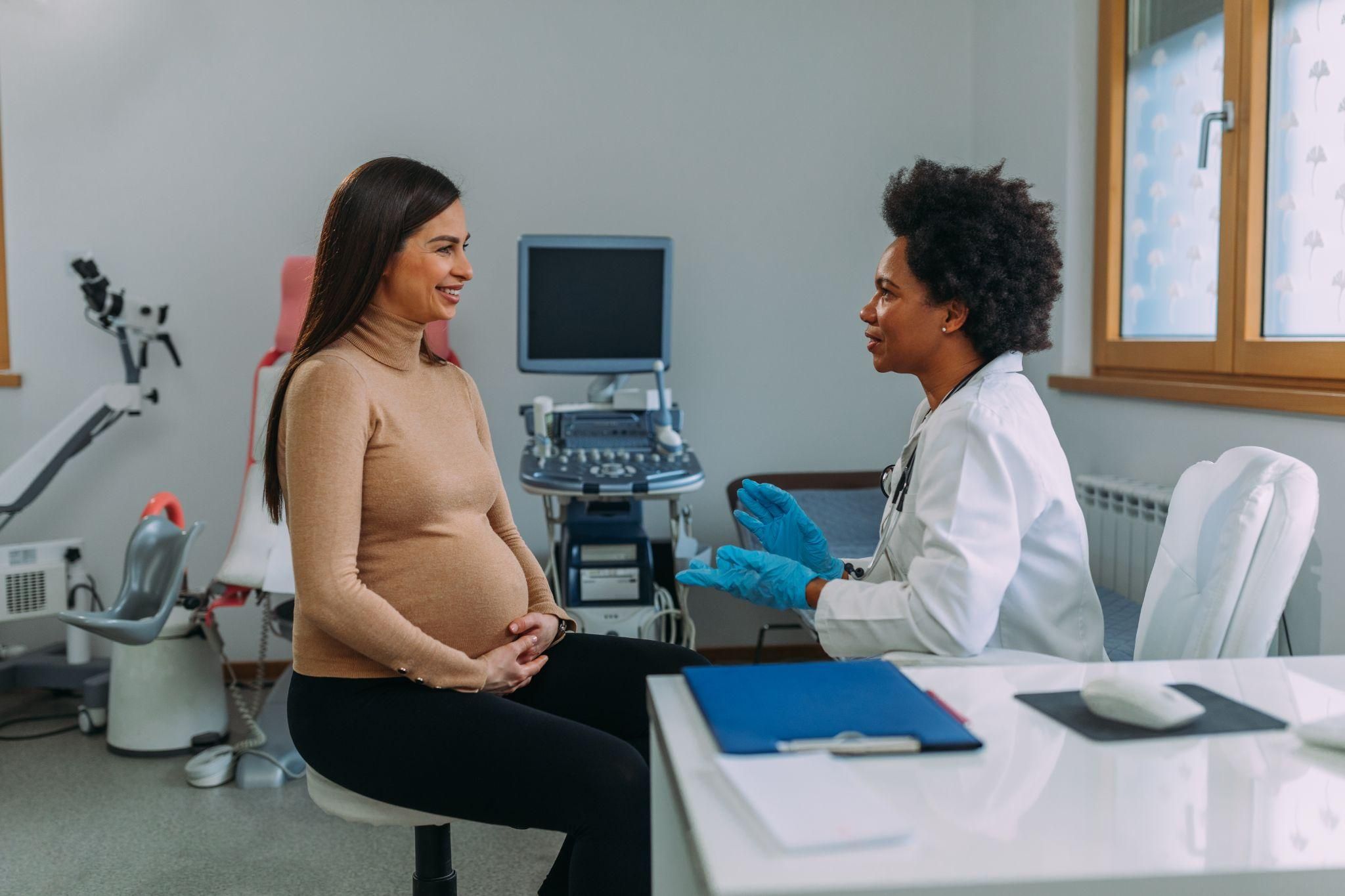 Obstetrician discusses pregnancy health with pregnant woman during antenatal appointment.