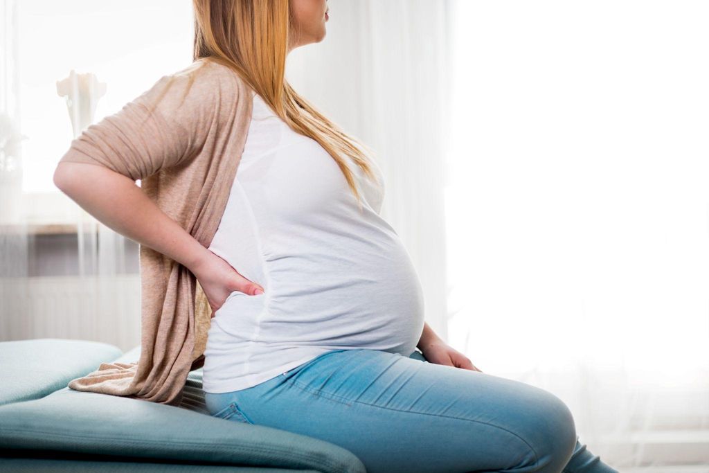 A pregnant woman rubbing her back due to poor antenatal posture.