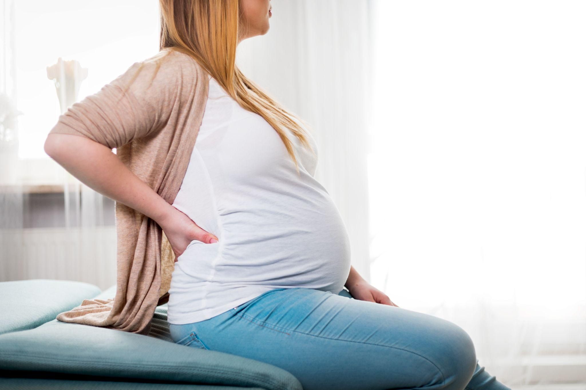 A pregnant woman rubbing her back due to poor antenatal posture.