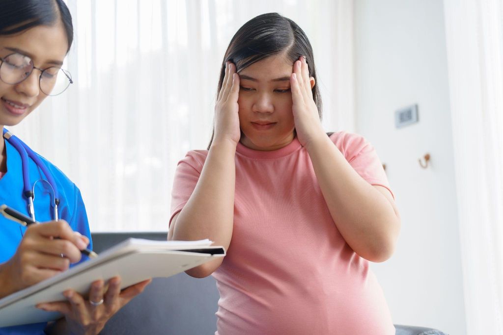 Pregnant woman puts head in hands during antenatal appointment, looking at medical record. Possible case of antenatal anxiety.