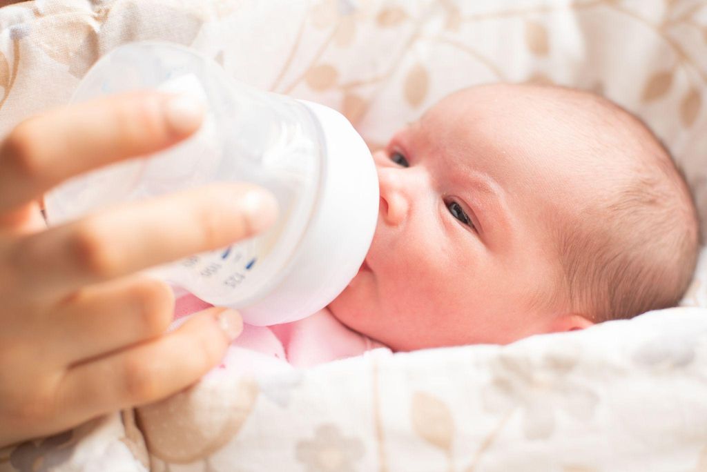 Woman bottlefeeds her newborn with expressed breast milk and colostrum.