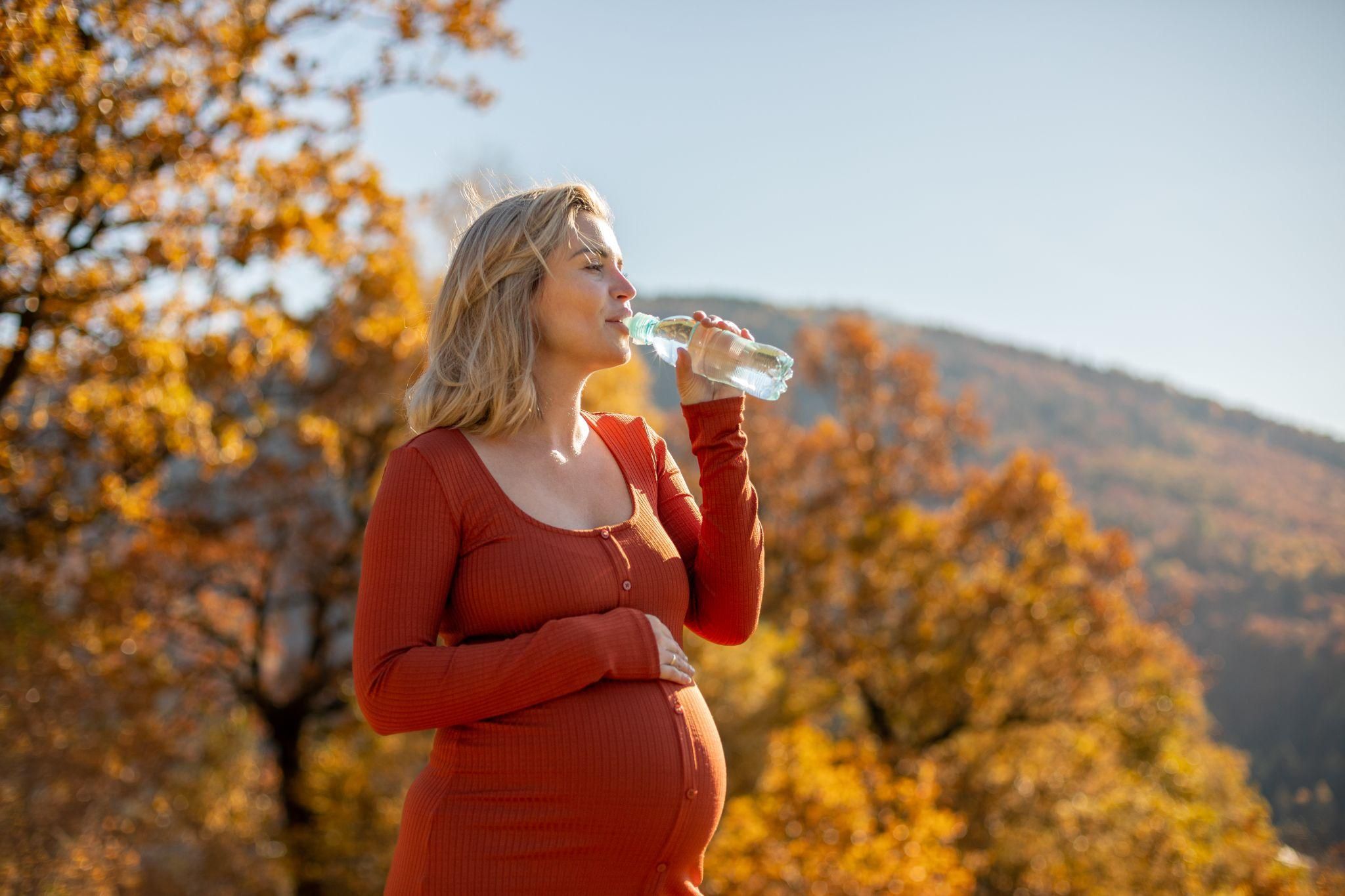 Pregnant woman drinks water during walk in her third trimester.