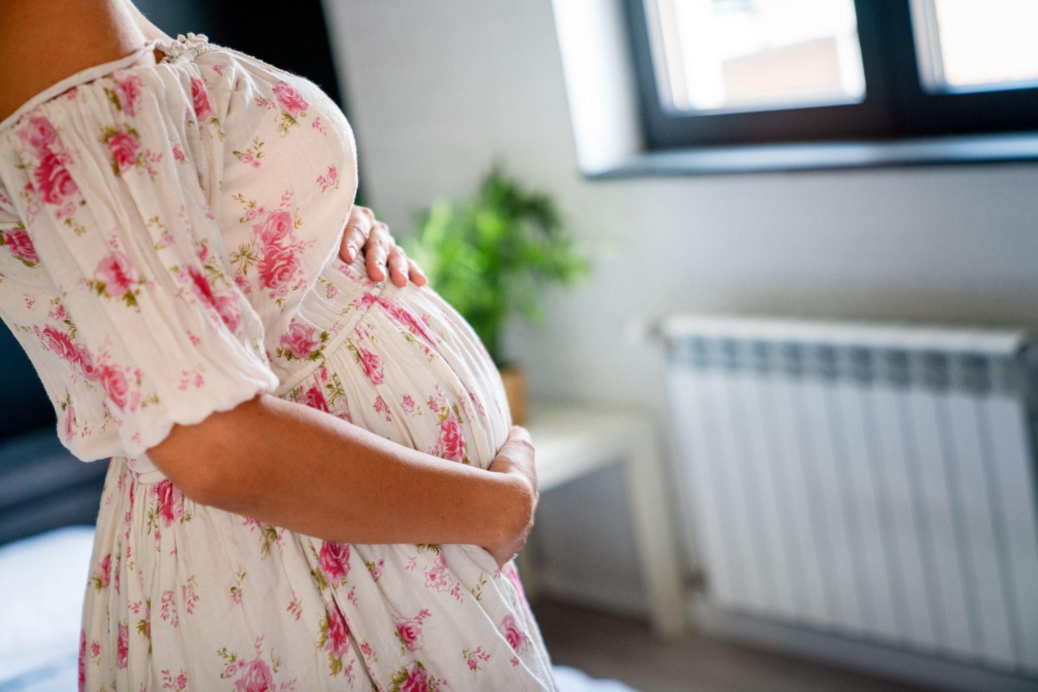 A mother-to-be cradling her twin baby bump, smiling softly.