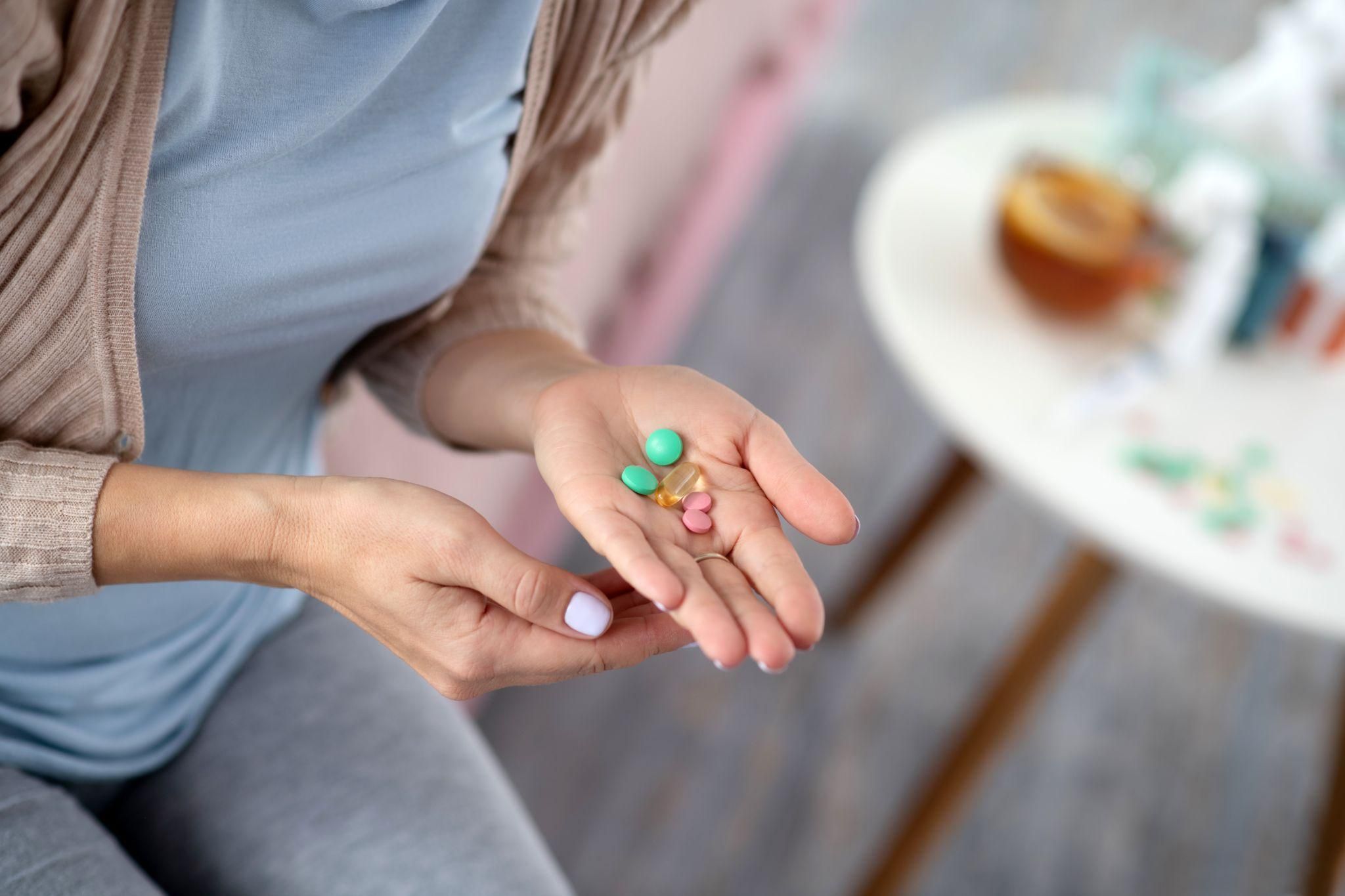 Pregnant woman holds handful of vitamin pills.