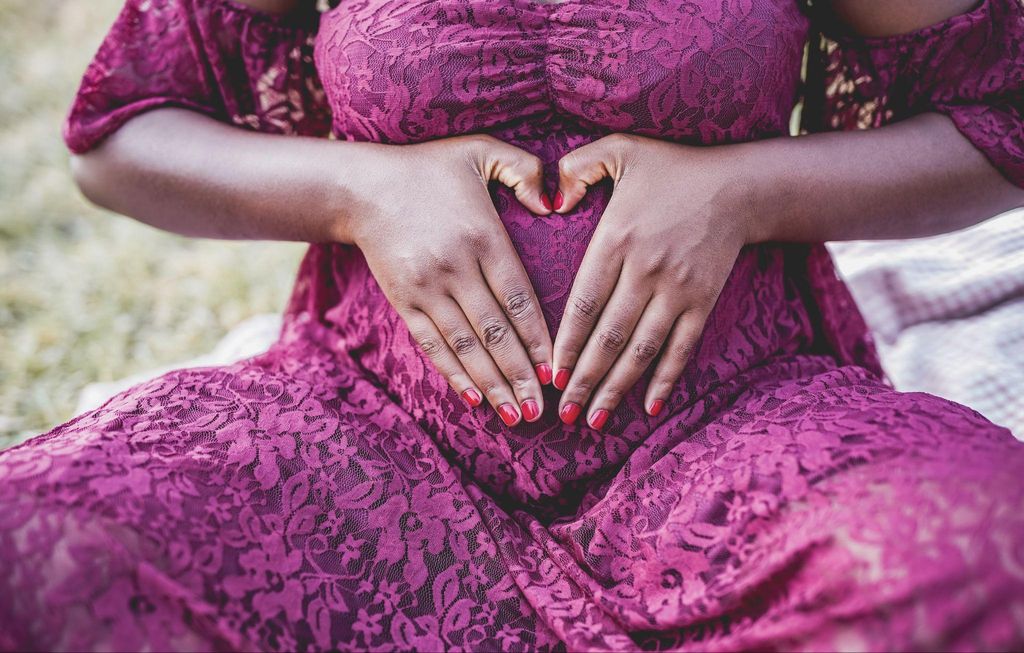 Pregnant woman puts manicured hands over bump in heart shape.