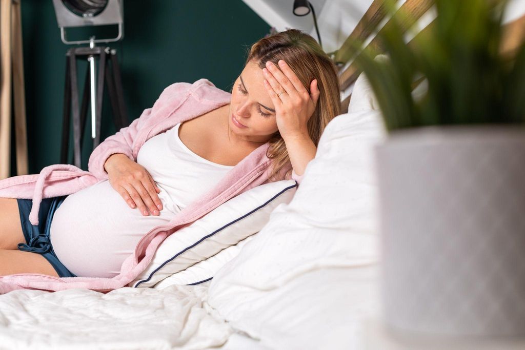 Pregant woman sits alone on bed looking sad. Possible case of antenatal depression.